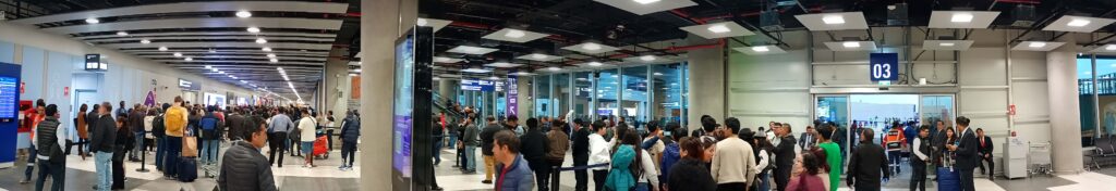 Panoramic view of the Jorge Chávez Airport international arrivals waiting area during peak hours in June 2025, showing a crowded scene with travelers, signs, and limited space.