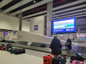 Interior view of Baggage Claim Area 5 at the new Jorge Chávez Airport in Lima, Peru, showing luggage scattered near the conveyor belt and a few passengers waiting nearby.